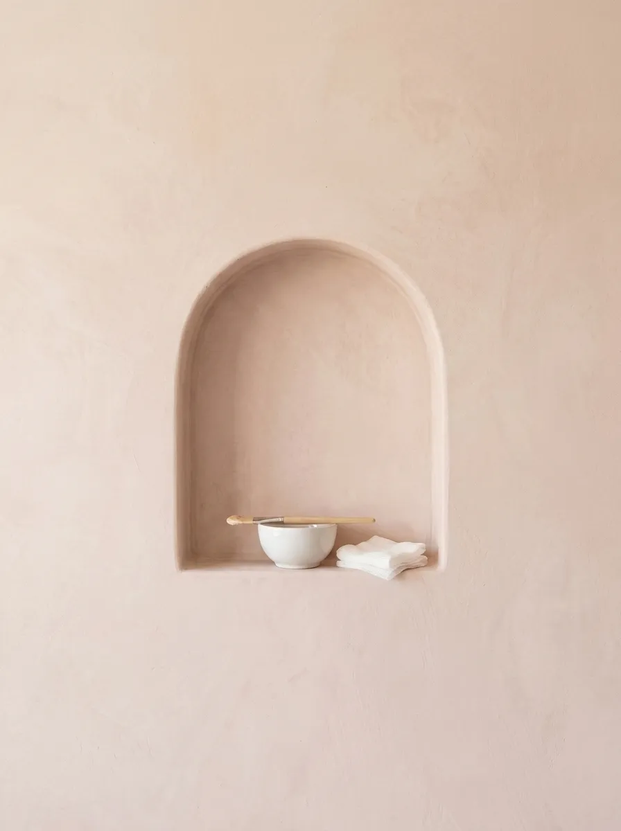 A plaster niche holding a ceramic bowl of enzyme masque with an applicator brush and gauze